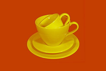 Two Different size of yellow ceramic tea cups with saucers on orange color background 