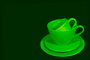 Two Different size of vivid green ceramic coffee cups with saucers on dark green background 