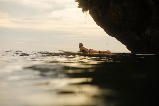 Side view of woman surfboarding in sea during sunset