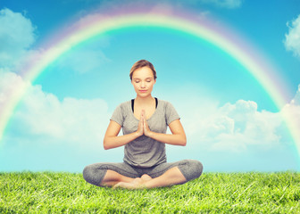 woman meditating in lotus yoga pose over rainbow 