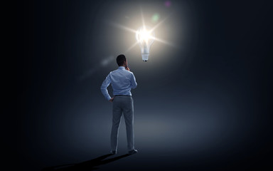 businessman looking at lighting bulb over dark
