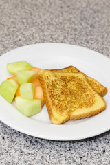 Vertical photograph of cooked French Toast with fruit on white plate placed on gray and black marble counter.  Copy space above.