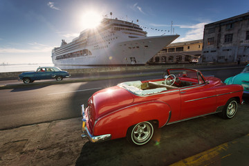 Old car on street of Havana at sunrise with cruise ship in background, Cuba