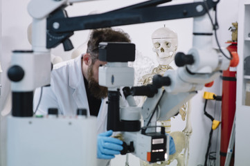 Scientist in laboratory that looks at microscope and a skeleton