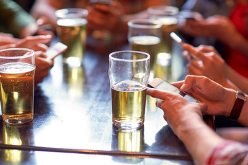 friends with beer and smartphones at bar or pub