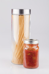 Jar of spaghetti sauce with dry pasta on a white surface. Canned sauce with spaghetti isolated on white background.