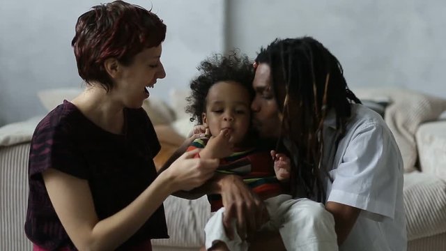 Affectionate mixed race parents kissing little son