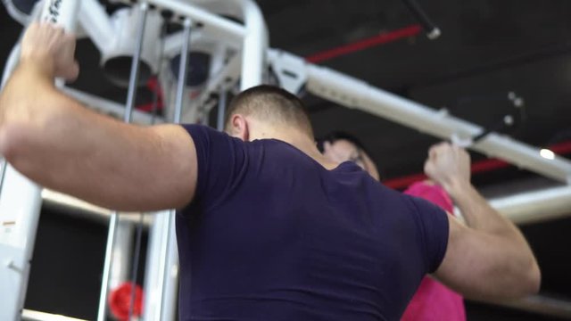 A young woman is engaged in a gym with a personal trainer. The fitness coach explains and shows the technique of doing the exercises. 4K