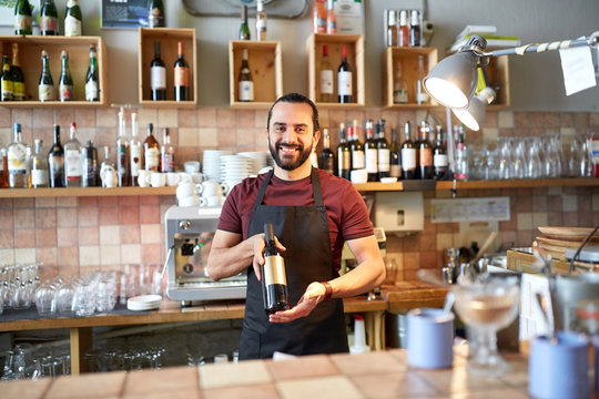 happy man or waiter with bottle of red wine at bar
