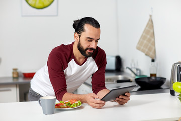 man with tablet pc eating at home kitchen