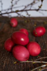 Easter eggs of red color on a wooden background, together with autumn branches