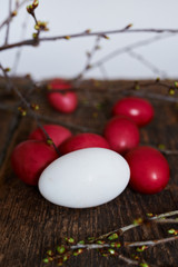 Easter eggs of red color on a wooden background, together with autumn branches