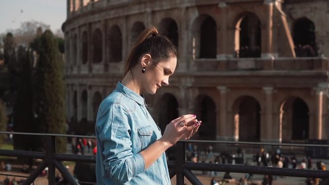 Young woman uses her smartphone in Rome, Italy against the background of Colosseum, looking a little sad. Slow motion.