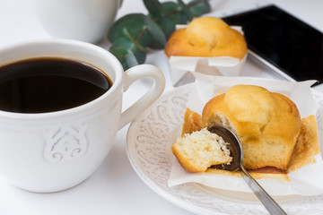 Cup of coffee, pastry on plate, smartphone, eucalyptus branch on white table, female business, style image for social media