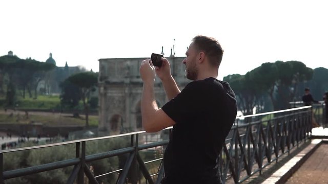Man tourist takes photos of landscapes in Rome, Italy on smartphone. The Konstantin s arch on background. Slow motion.