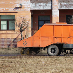 Orange urban sweeper cleans road from dirt with a round brush in the spring.
