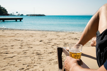 Man sitting on the beach holding glass beer