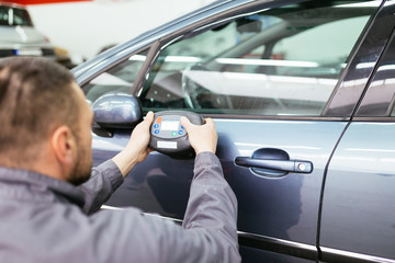 Man using car color meter to check color shade of car. Selective focus on hand.