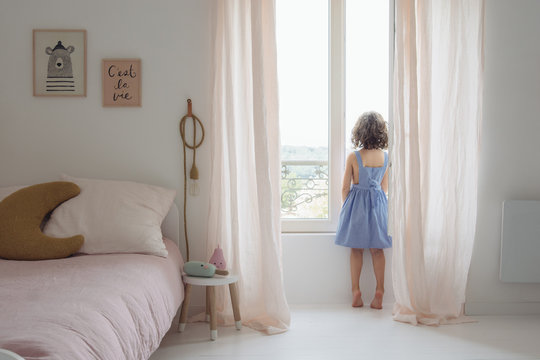 petite fille qui regarde par la fenêtre dans sa chambre
