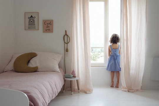 petite fille qui regarde par la fen&ecirc;tre dans sa chambre