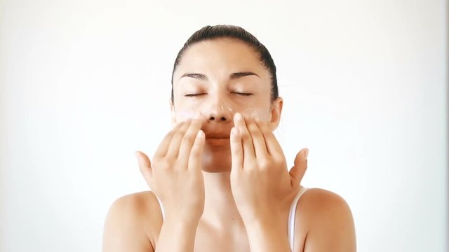 Beautiful brunette woman applying cream on her face