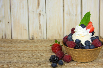 fresh berries on ice cream with whipped cream and mint leaf in waffle bowl