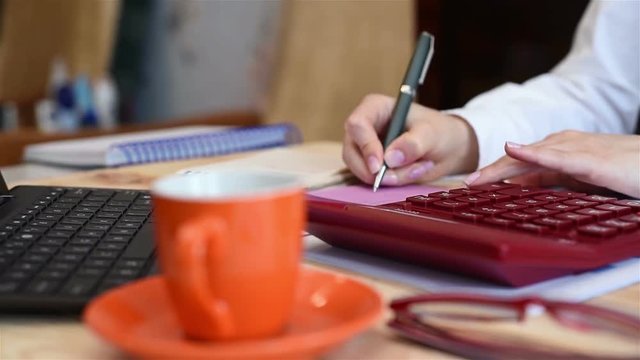 Businesswoman Compiles Statistics On  Calculator And Writes Data To Paper