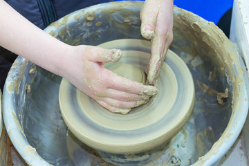 The master teaches the child, a student of pottery. Helps to make out of clay on a Potter's wheel a small jug.