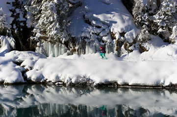 Woman running in snowshoes around a snowy winter alpine lake.