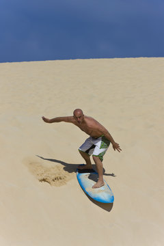 A Surfer Sand Boarding His Way Down A Dune On The Way To The Ocean.