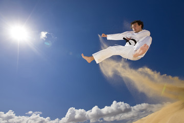 Marital artist in flying kick from dunes.