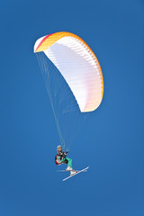 A female paraglider pilot flying her glider with skis on for take off landing in snowy mountains.