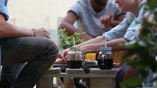 Mid-section view of young people sitting around table eating pizza and drinking cocktails