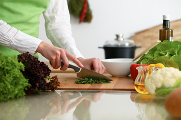 Closeup of human hands cooking vegetables salad in kitchen on the glassr table with reflection. Healthy meal and vegetarian concept