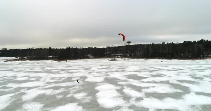 Ice parasailing, Cinema 4k aerial view of a red parachute sailer turning infront of Haukilahti coast, on a cloudy day, at the baltic sea, in Haukilahti, Espoo, Finland