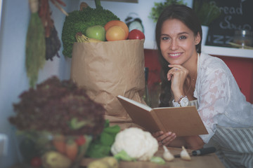 Young woman reading cookbook in the kitchen, looking for recipe