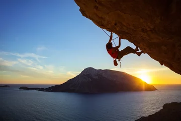 Deurstickers Young man climbing overhanging cliff at sunset © Andrey Bandurenko