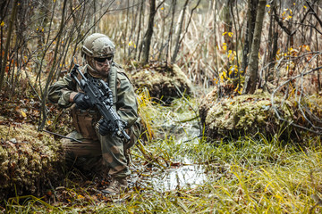 Norwegian Rapid reaction special forces FSK soldier sitting on the swamp. Field camo uniforms, combat helmet and eye-wear goggles are on
