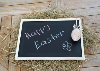 Chalkboard with text Happy Easter and Decorative egg on dry grass and a wooden background