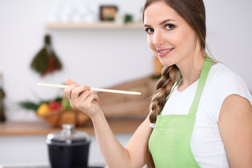 Young  woman is  cooking in a kitchen. Housewife is tasting the soup by wooden spoon.