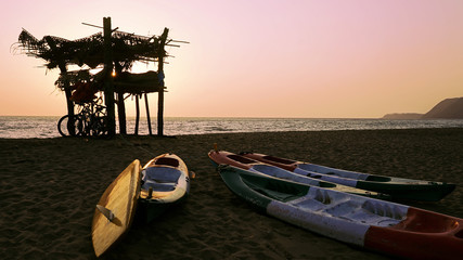 Beautiful scene of the sun setting over the ocean with boats and rescue service watch tower in...