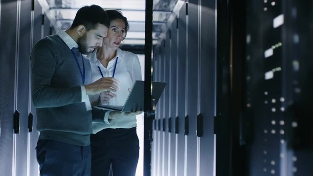  Male IT Specialist Holds Laptop and Discusses Work with Female Server Technician. They're Standing in Data Center, Rack Server Cabinet is Open. Shot on RED EPIC-W 8K Helium Cinema Camera.