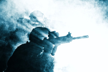 Black silhouettes of pair of soldiers in the smoke moving in battle operation. Back light, cropped,...