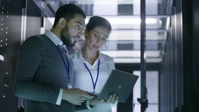 Male and Female Server Engineers Work on a Laptop in Data Center. He Opens Rack Server Cabinet. Shot on RED EPIC-W 8K Helium Cinema Camera.