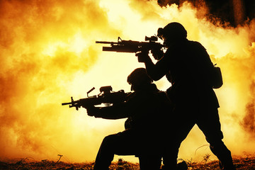 Black silhouettes of pair of soldiers in the smoke fire burning moving in battle operation. Back...