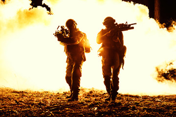 Black silhouettes of pair of soldiers in the smoke fire burning moving in battle operation. Back...