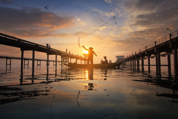 Fototapeta na wymiar Silhouette of fishermen using nets to catch fish at the Bangpra lake with beautiful scenery of nature during sunrise time. Bang Pra Reservoir at Chonburi province in Thailand