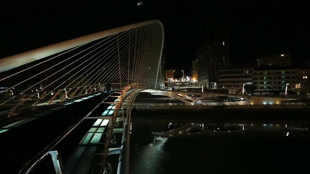 People walking Zubizuri bridge, illuminated night cityscape of Bilbao, panorama