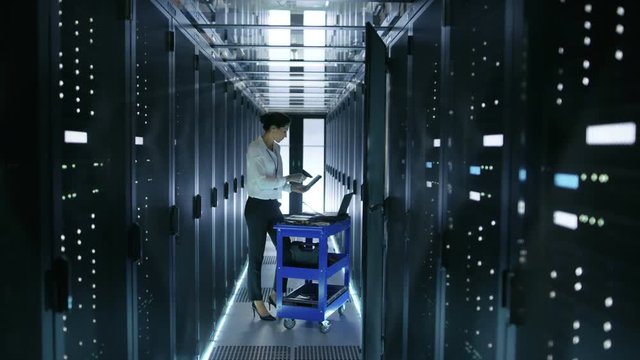 Female IT Engineer Works on a Laptop and Scans Hard Drives That are Lying on a Cart. She Works in Data Center. Shot on RED EPIC-W 8K Helium Cinema Camera.