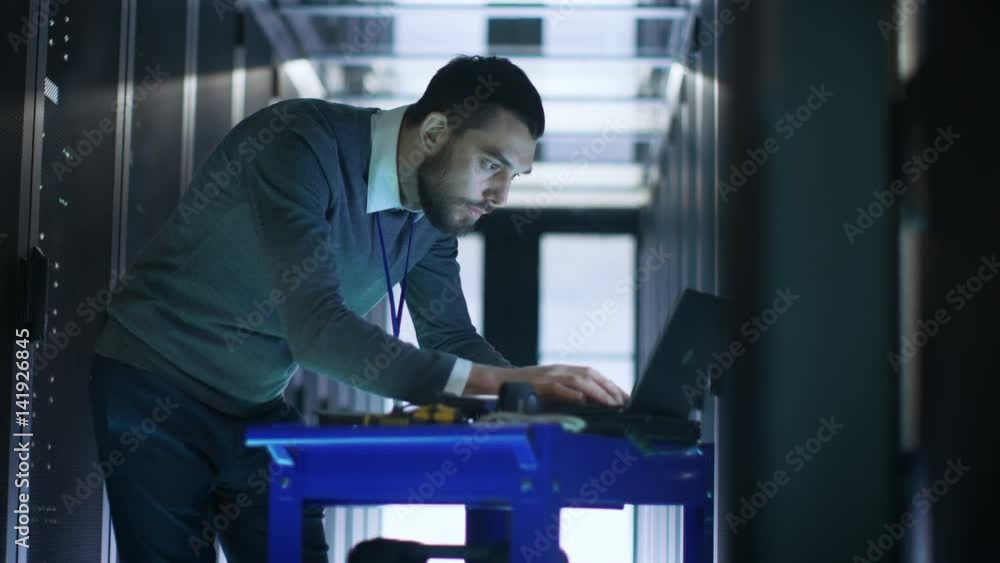 Poster it engineer with crash cart working on a laptop computer in working data center full of rack servers